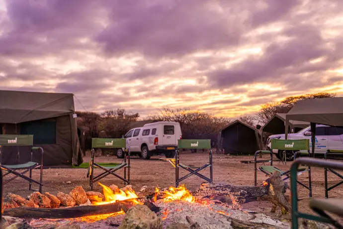Campsite at sunset with tents, camp chairs and a fire